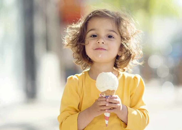 shutterstock_137446895 A young child with curly hair holding an ice cream cone outdoors