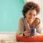 Gut Bacteria Bombshell Rattles Coffee Drinkers Everywhere A woman lying on a cushion with a coffee cup, smiling at the camera