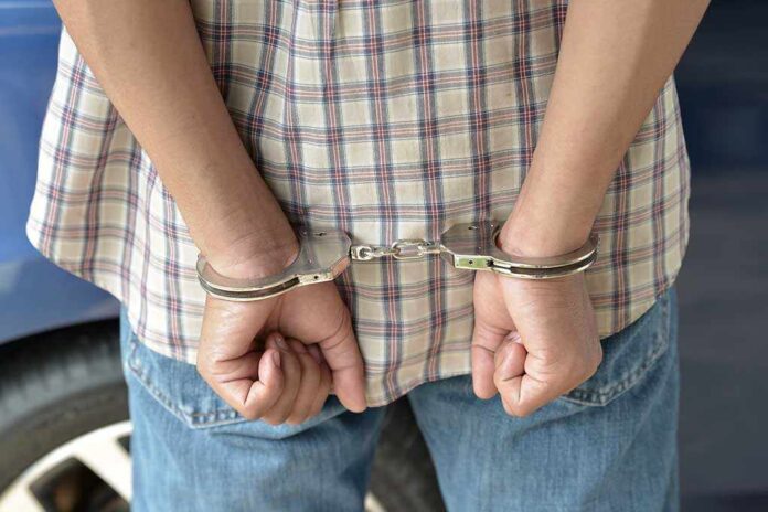 A person in handcuffs viewed from behind, wearing a plaid shirt and denim jeans