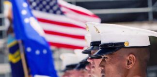 U.S. Marines in uniform standing in formation with flags in the background