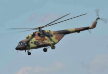 Apache Down Near Hormuz—Was It Fire or Failure? Camouflage military helicopter in flight against blue sky.