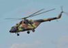 Mystery Apache Crash Near Hormuz Stirs Nerves Camouflage military helicopter in flight against blue sky.