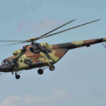 Mystery Apache Crash Near Hormuz Stirs Nerves Camouflage military helicopter in flight against blue sky.