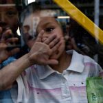 A child playfully covering their face while looking through a glass window