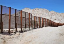 Border Wall Threatens Land Owners A long border wall stretches across a desert landscape with mountains in the background