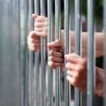 ICE Attack Fallout: 450 Years Hands gripping metal prison bars