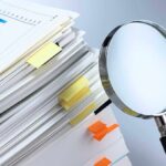 Stack of documents with a magnifying glass beside it
