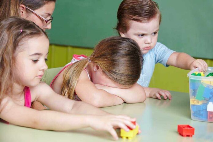 Children,Playing,With,Basketball,And,Getting,Comfort,From,Nursery,Teacher Children at a table with building blocks, one child appears upset