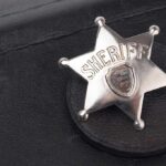Badge-Toting Predator Exposed A silver sheriff badge resting on a black leather surface