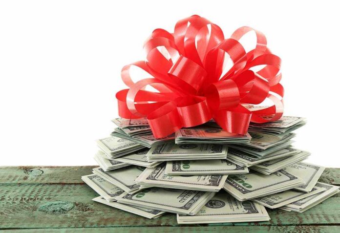 Pile,Of,Dollars,With,Bow,As,Gift,Isolated,On,White A stack of cash topped with a red ribbon bow