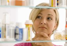 A woman thoughtfully looking at a medicine cabinet filled with various medications
