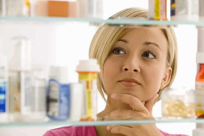 A woman thoughtfully looking at a medicine cabinet filled with various medications