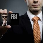 Kids’ Meal Millions Vanish — FBI Pounces Abroad A man in a suit holding an FBI identification card while making a shushing gesture