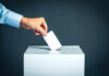 Hand placing ballot into voting box.