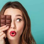 Bionic Eye Approved—Seniors Reads Again Woman holding chocolate bar over one eye against teal background