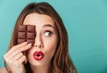 Woman holding chocolate bar over one eye against teal background