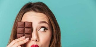 Woman holding chocolate bar over one eye against teal background