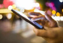 A persons hand using a smartphone in a city at night with blurred lights in the background