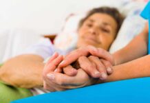 A caregiver holding the hands of an elderly patient in a hospital bed