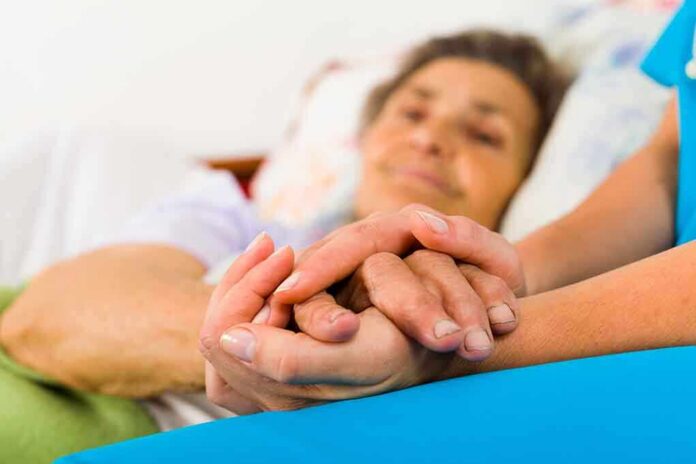 shutterstock_161459273 A caregiver holding the hands of an elderly patient in a hospital bed