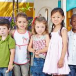 YMCA Scrubs Gender Pledge — Why Now? Five children standing together in a playground setting, smiling at the camera