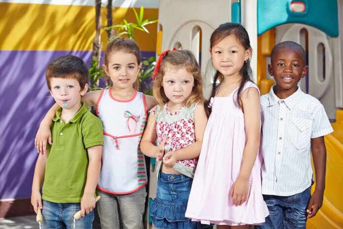 shutterstock_193504529 Five children standing together in a playground setting, smiling at the camera