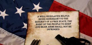 A revolver and bullets placed on an aged document with the Second Amendment text, set against an American flag background
