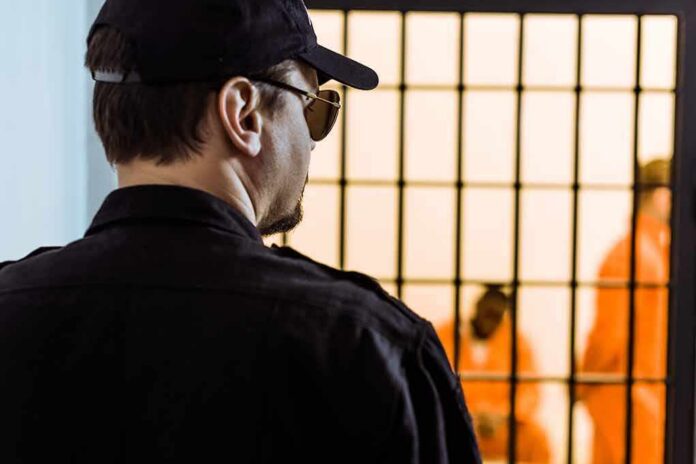 shutterstock_1030269964 Security guard watching inmates behind jail bars