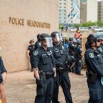 Police officers in riot gear stand in formation outside a headquarters building