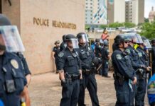 FBI Pounces After Chilling Trump Threat Police officers in riot gear stand in formation outside a headquarters building