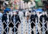 Police officers in masks stand behind portable barricades on a city street
