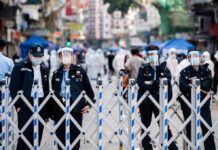 Police officers in masks stand behind portable barricades on a city street