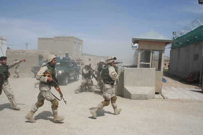 shutterstock_1931171405 Soldiers in desert uniforms run past a checkpoint amid dust