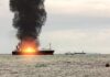 Cargo ship on fire with thick black smoke at sea