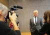 Man in a gray suit speaks to a reporter during an interview