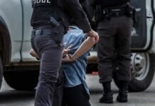 Police officer detaining a handcuffed person beside a vehicle