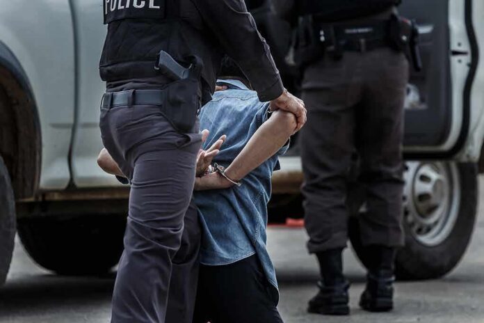 Police officer detaining a handcuffed person beside a vehicle