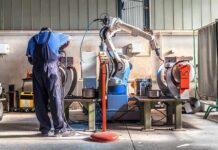 Factory worker operates near an industrial robot arm in a workshop