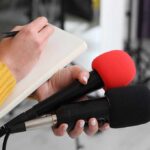 25-Year Delay Exposed: Sunscreen Stuck In 1990s Journalist holding two microphones while writing in a notebook