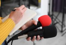 HealthCare Jobs Surge While Others Stall Journalist holding two microphones while writing in a notebook