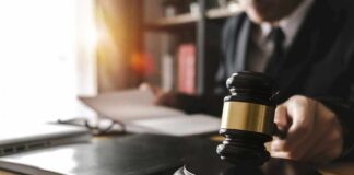 Judge's gavel on desk with person reading documents in background