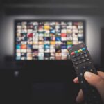 Hand holding TV remote toward a screen with streaming thumbnails