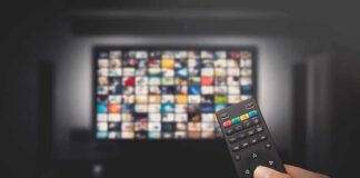 Hand holding TV remote toward a screen with streaming thumbnails