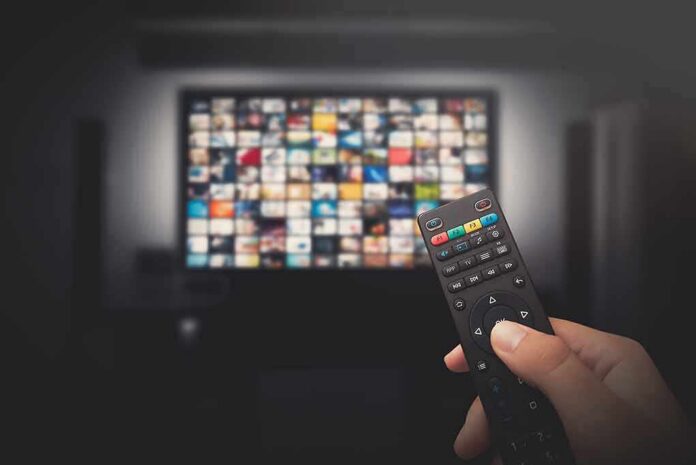 shutterstock_1439344193-1 Hand holding TV remote toward a screen with streaming thumbnails