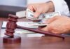 A person counting cash in a courtroom setting with a gavel in the foreground