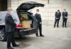 Mystery Donor Fast-Tracks Cremation Pallbearers beside a hearse with a coffin and flowers