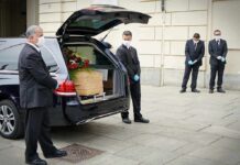 Pallbearers beside a hearse with a coffin and flowers