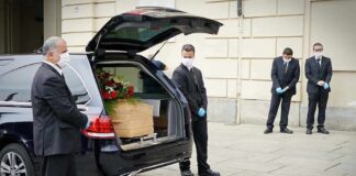 Pallbearers beside a hearse with a coffin and flowers