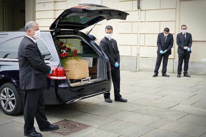 shutterstock_1738919135 Pallbearers beside a hearse with a coffin and flowers