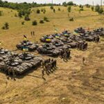 Rows of military tanks with soldiers assembled on a dry field